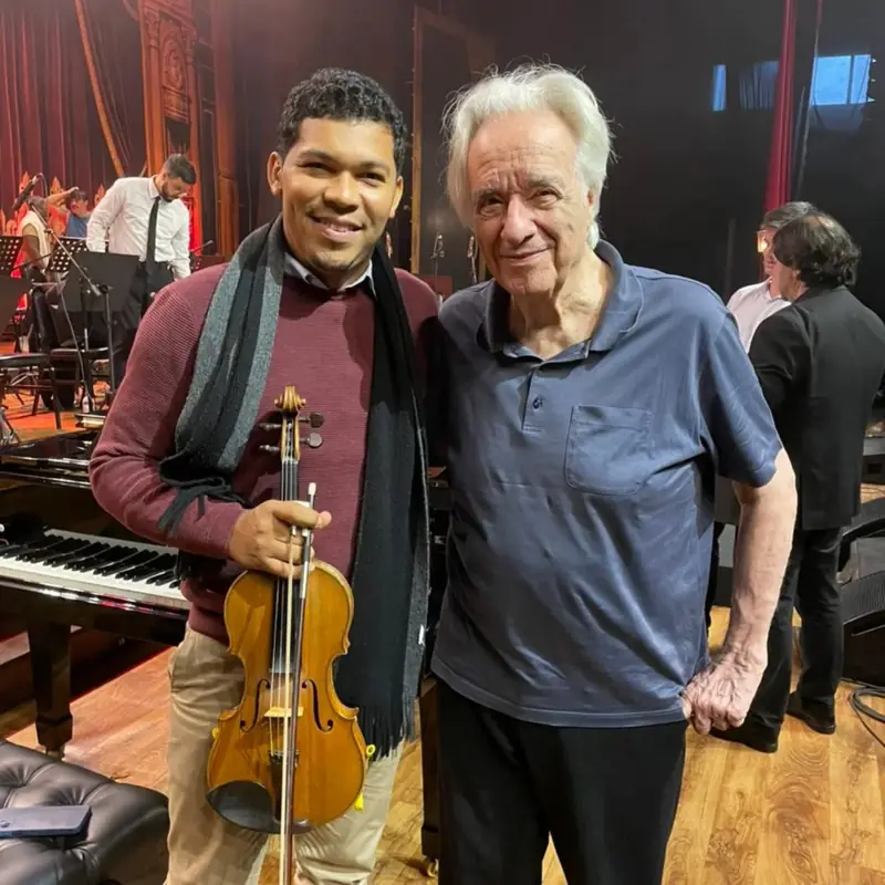 Violinista com músico nos bastidores com piano ao fundo